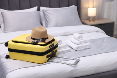 Photo of Suitcase with hat and sunglasses on bed in hotel room