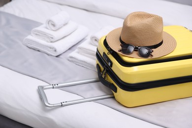 Photo of Suitcase with hat and sunglasses on bed in hotel room