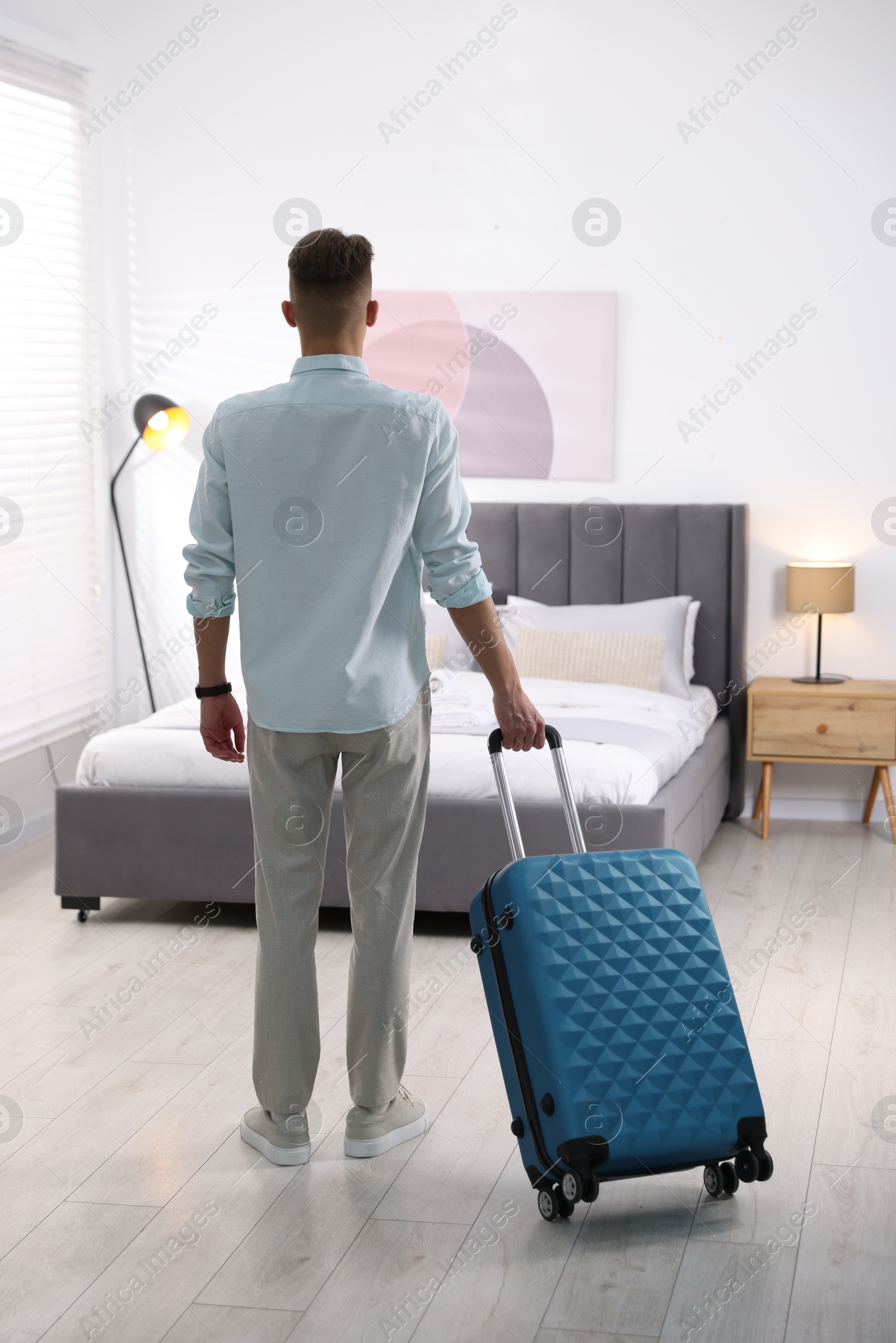 Photo of Man with suitcase in hotel room, back view