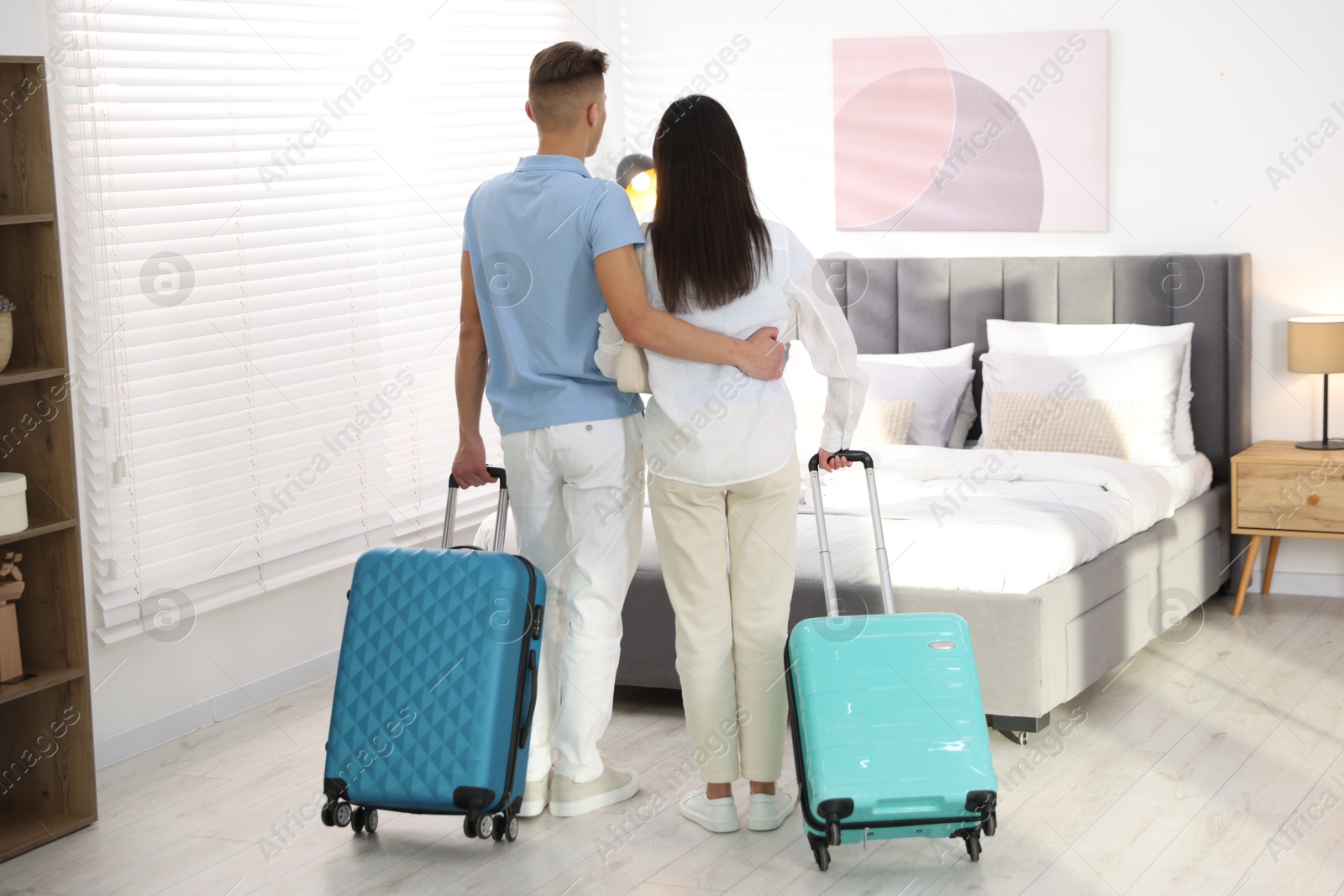 Photo of Happy couple with suitcases in hotel room, back view