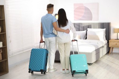 Photo of Happy couple with suitcases in hotel room, back view