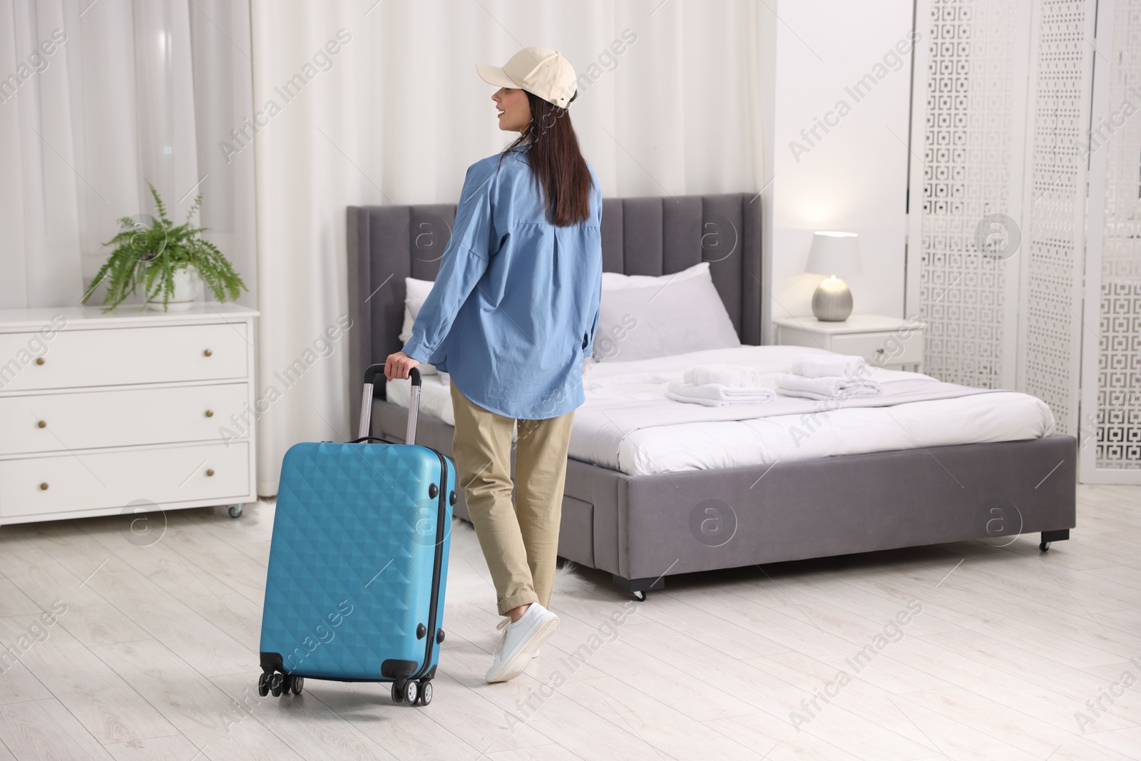 Photo of Woman with suitcase in hotel room, back view