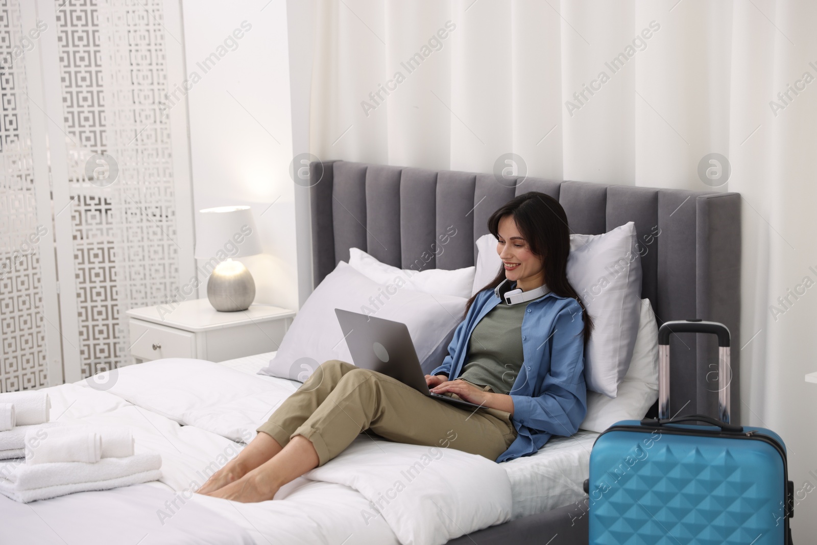 Photo of Woman with laptop on bed in her hotel room. Space for text