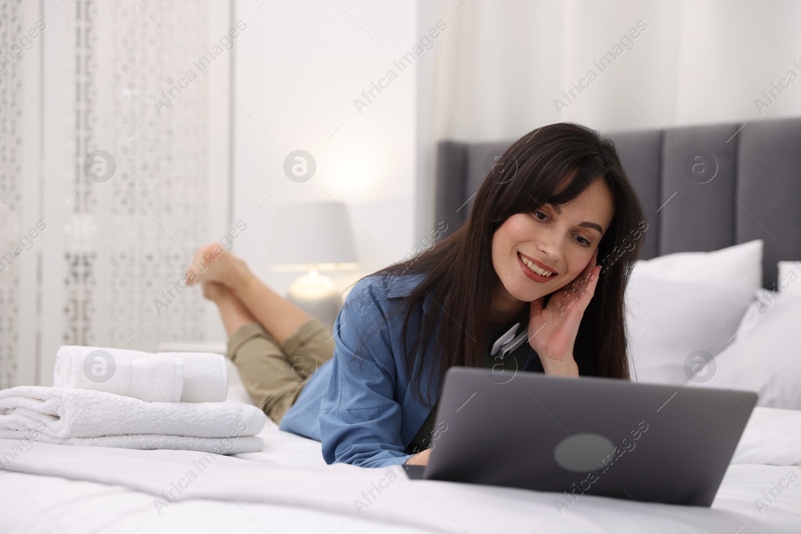 Photo of Woman with laptop on bed in her hotel room. Space for text