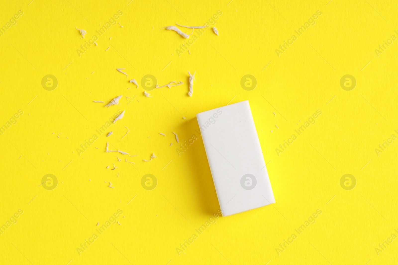 Photo of One eraser and scraps on yellow background, top view