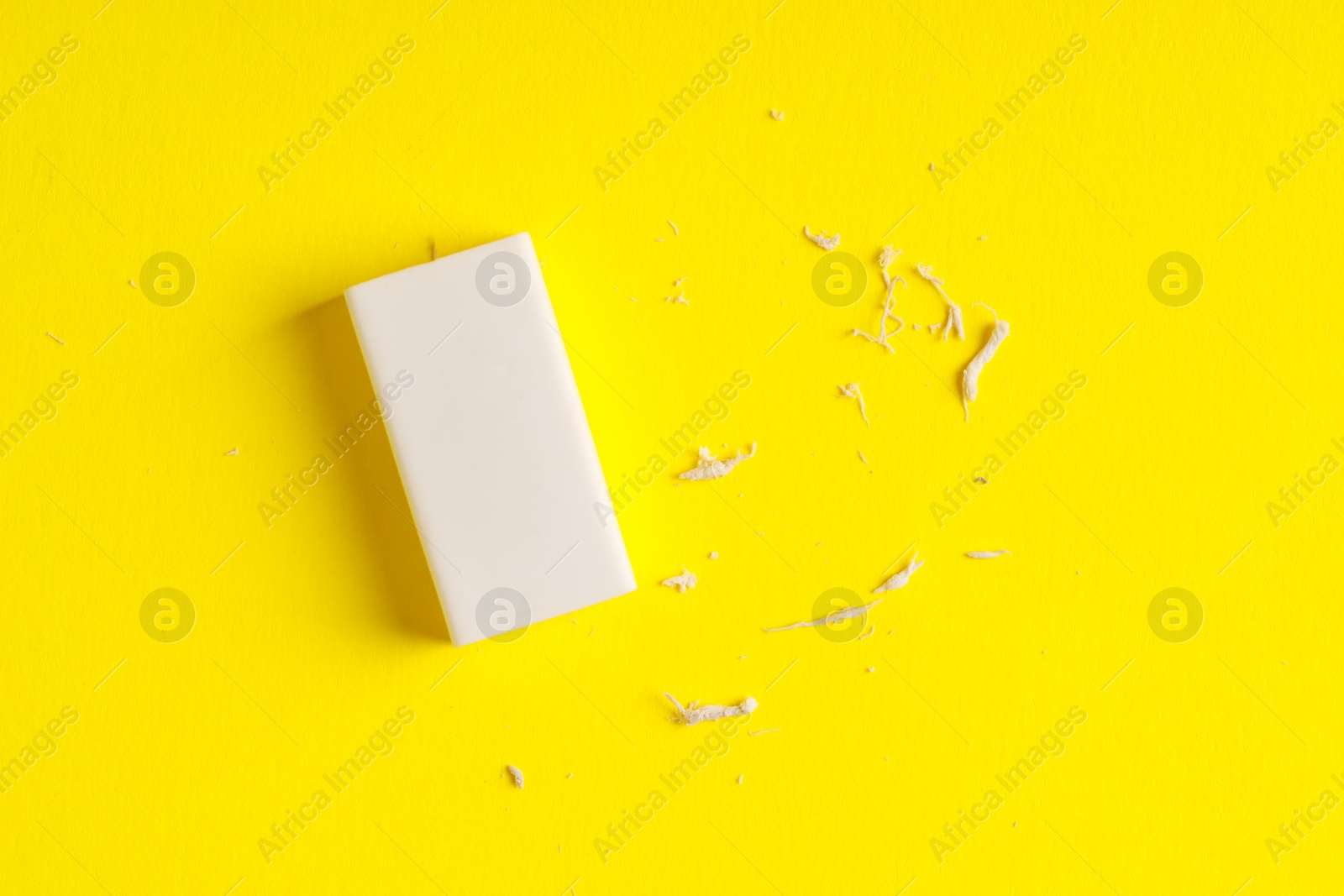 Photo of One eraser and scraps on yellow background, top view