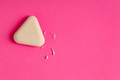 Photo of One eraser and scraps on pink background, top view. Space for text