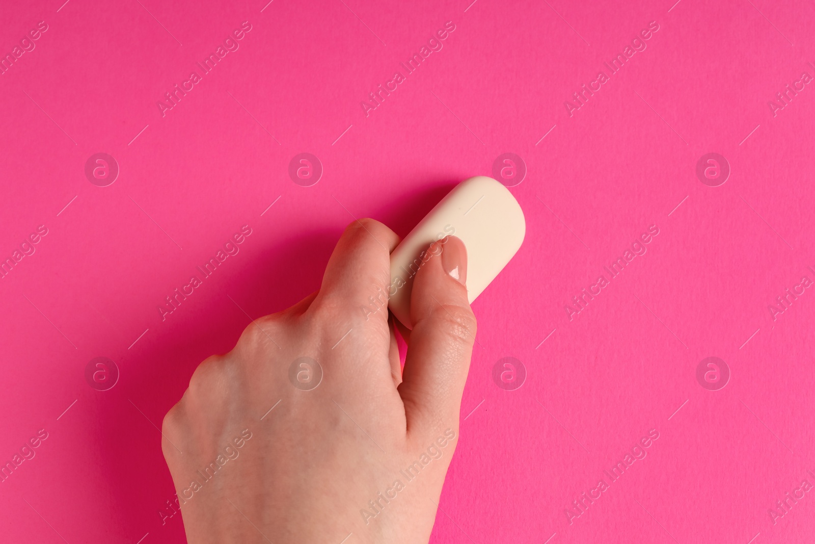 Photo of Woman using eraser on pink background, closeup