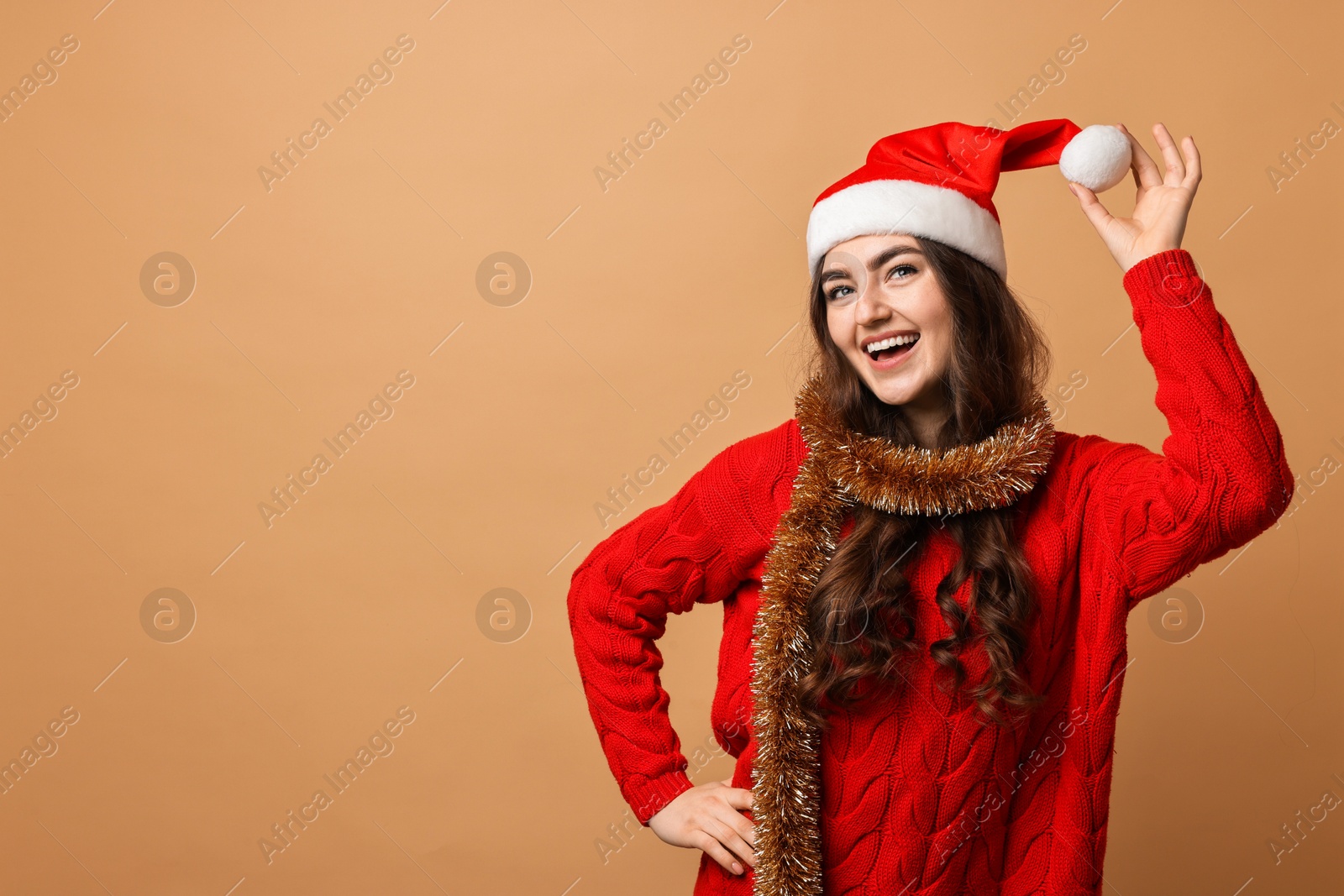 Photo of Happy young woman with tinsel and Santa hat on beige background. Space for text