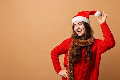 Photo of Happy young woman with tinsel and Santa hat on beige background. Space for text