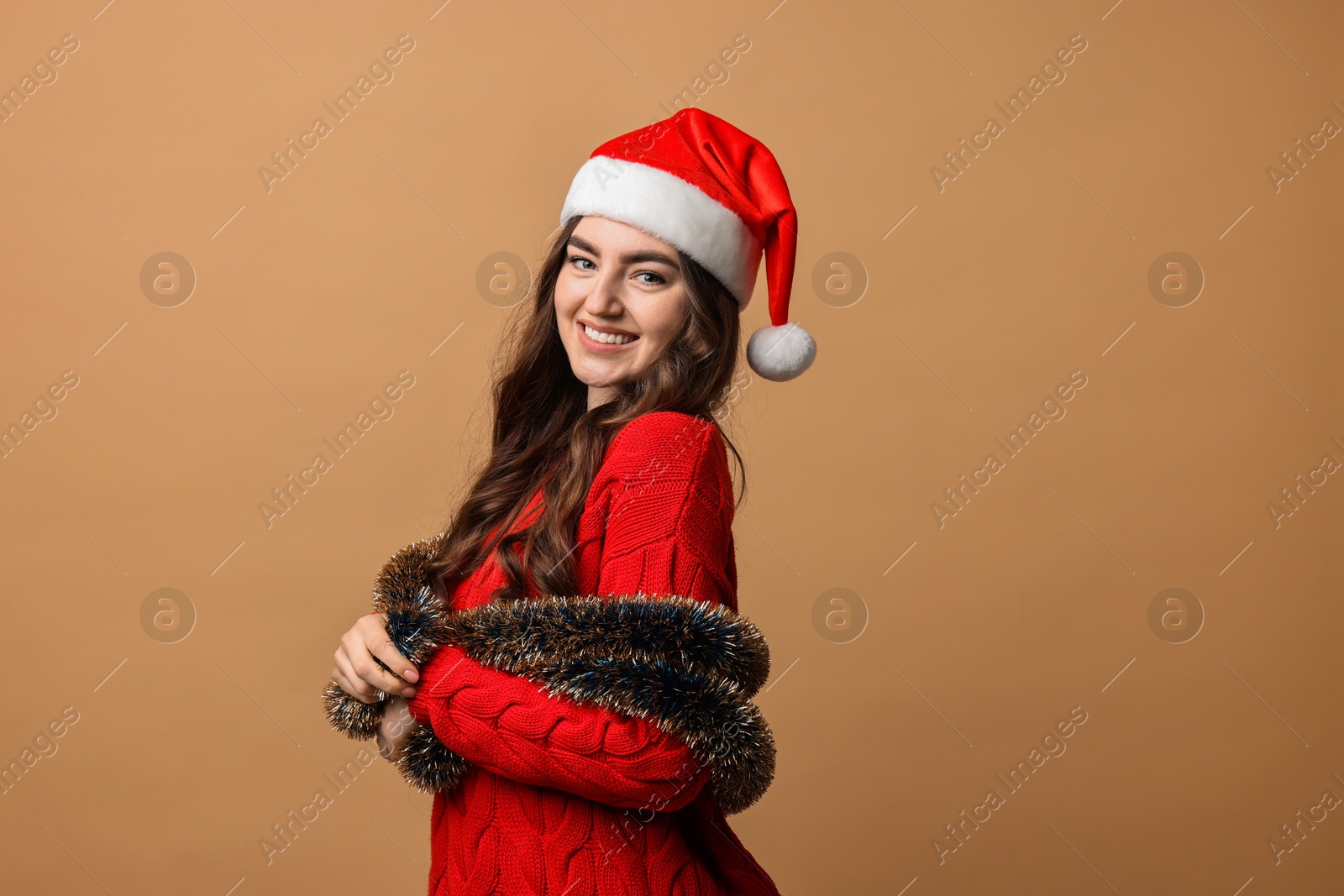 Photo of Happy young woman with tinsel and Santa hat on beige background. Space for text