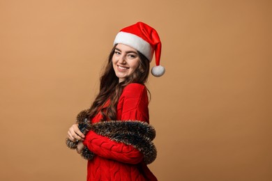 Photo of Happy young woman with tinsel and Santa hat on beige background. Space for text