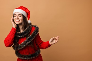 Photo of Happy young woman with tinsel and Santa hat on beige background. Space for text