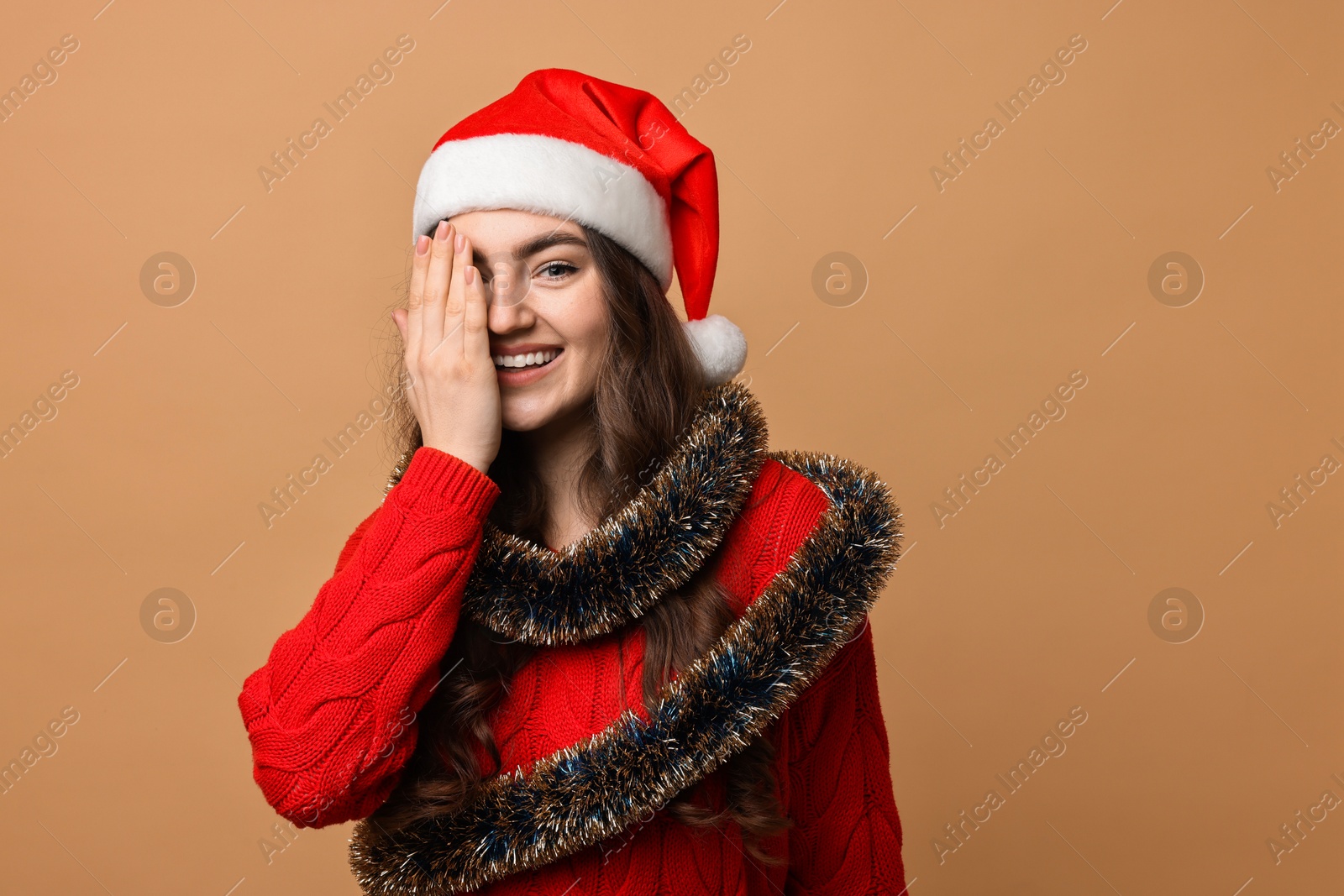 Photo of Happy young woman with tinsel and Santa hat on beige background. Space for text