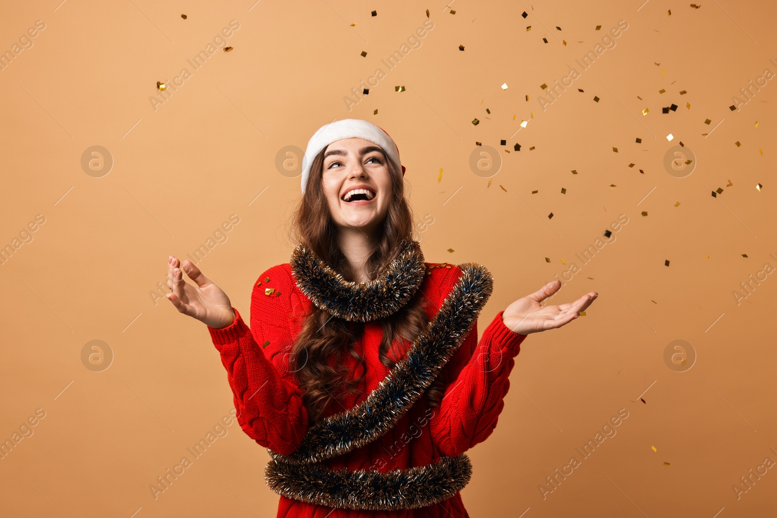 Photo of Happy young woman with tinsel under falling confetti on beige background