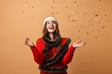 Photo of Happy young woman with tinsel under falling confetti on beige background