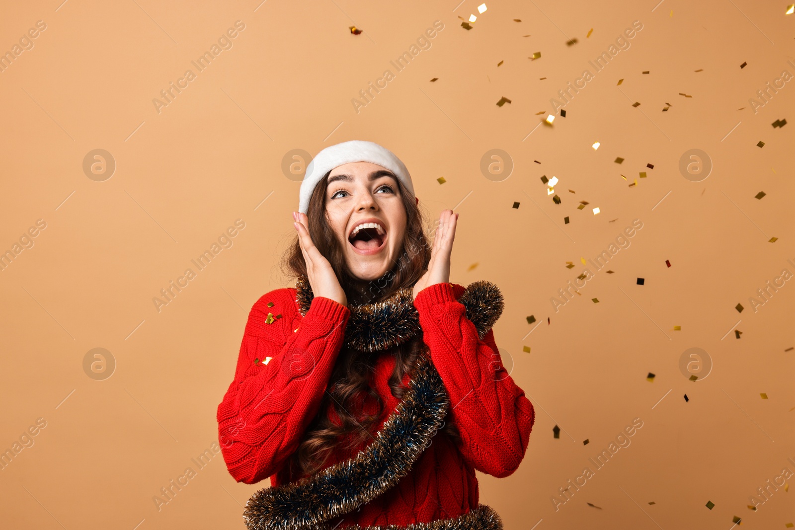 Photo of Emotional young woman with tinsel and falling confetti on beige background