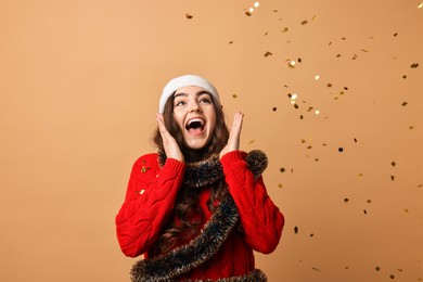 Photo of Emotional young woman with tinsel and falling confetti on beige background