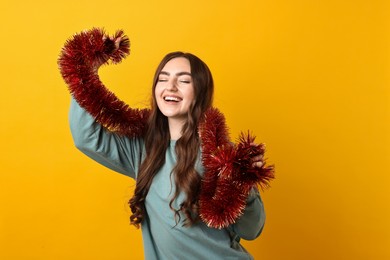 Photo of Happy young woman with tinsel on orange background. Space for text