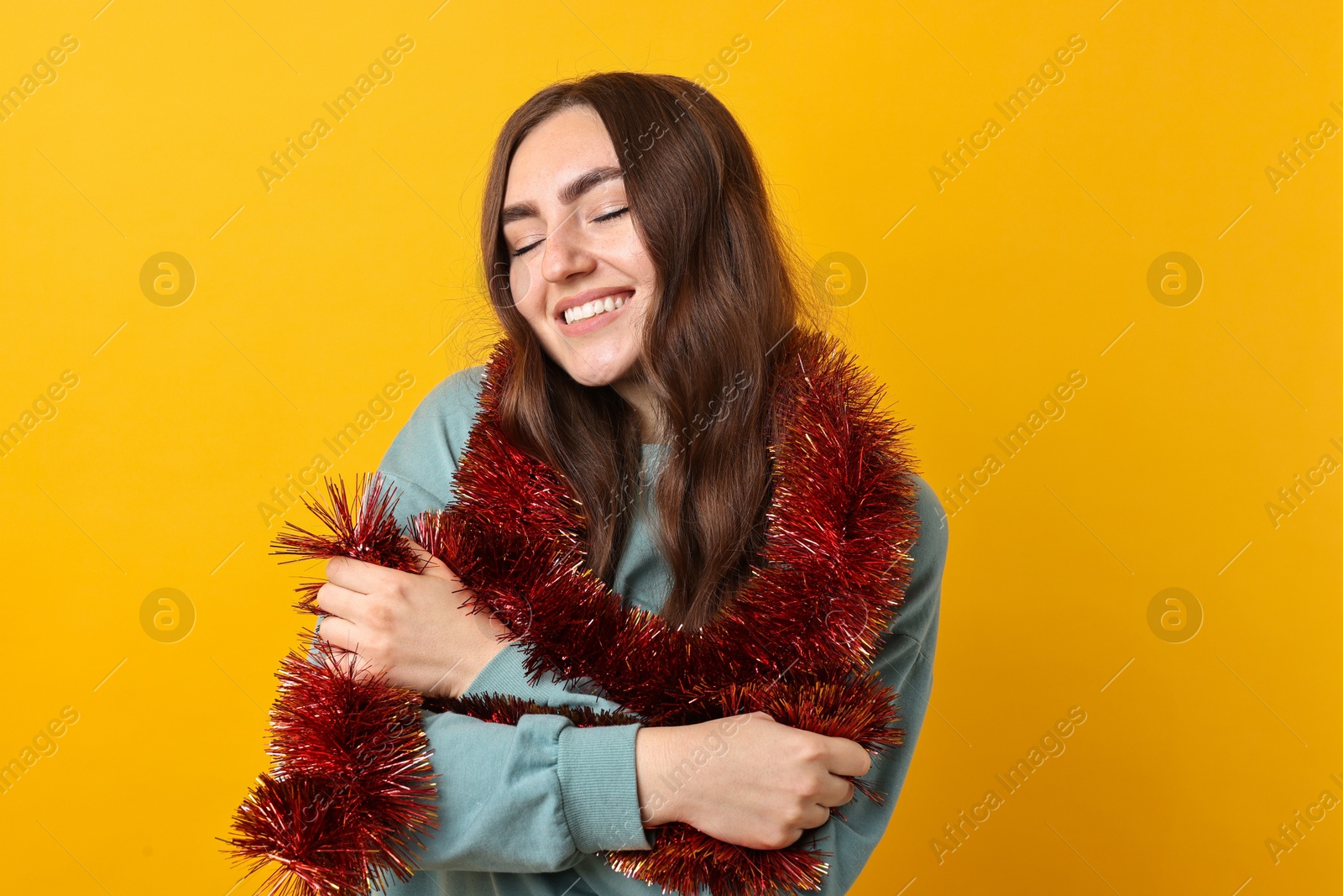 Photo of Happy young woman with tinsel on orange background