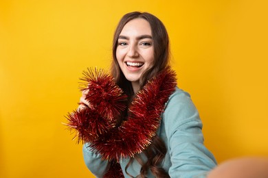 Photo of Happy young woman with tinsel taking selfie on orange background