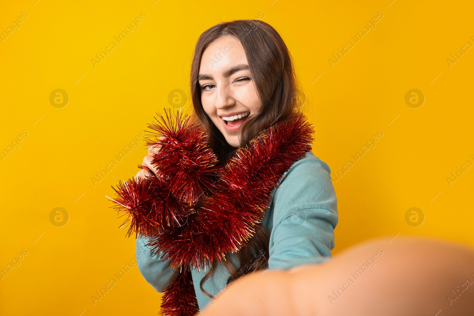 Photo of Happy young woman with tinsel taking selfie on orange background