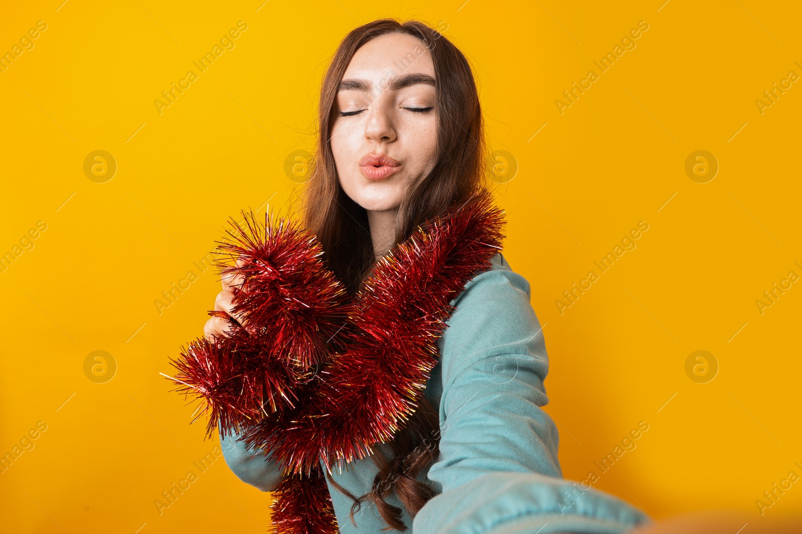 Photo of Happy young woman with tinsel taking selfie on orange background