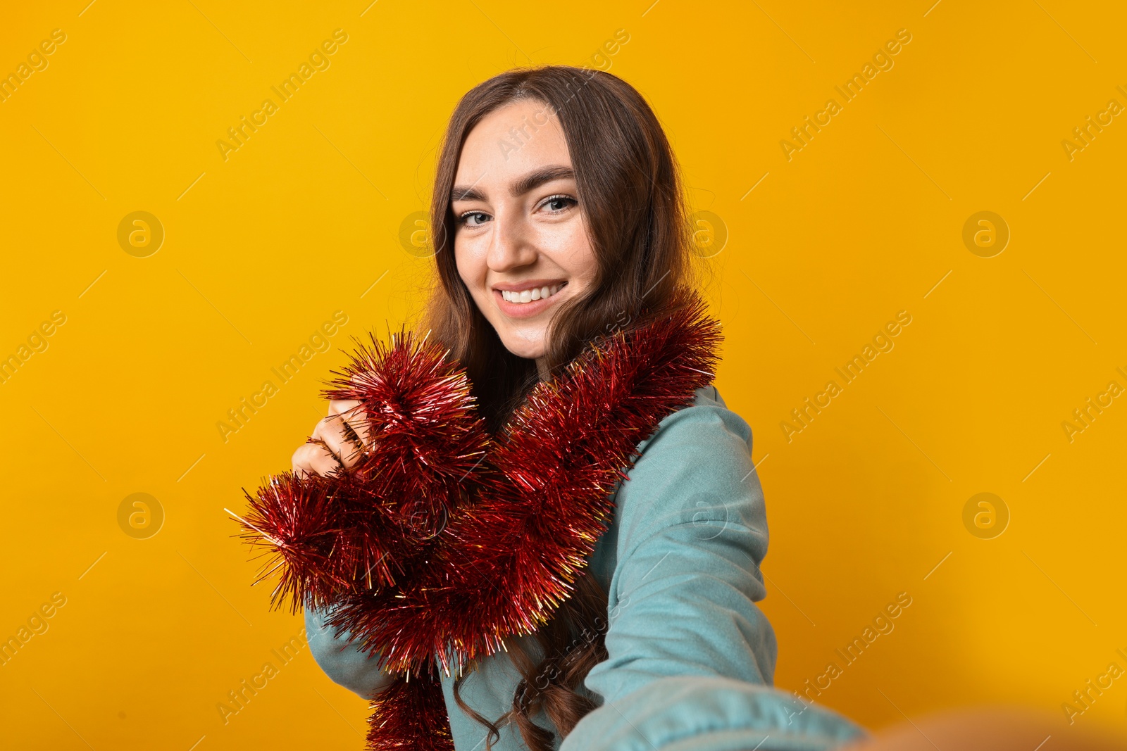 Photo of Happy young woman with tinsel taking selfie on orange background