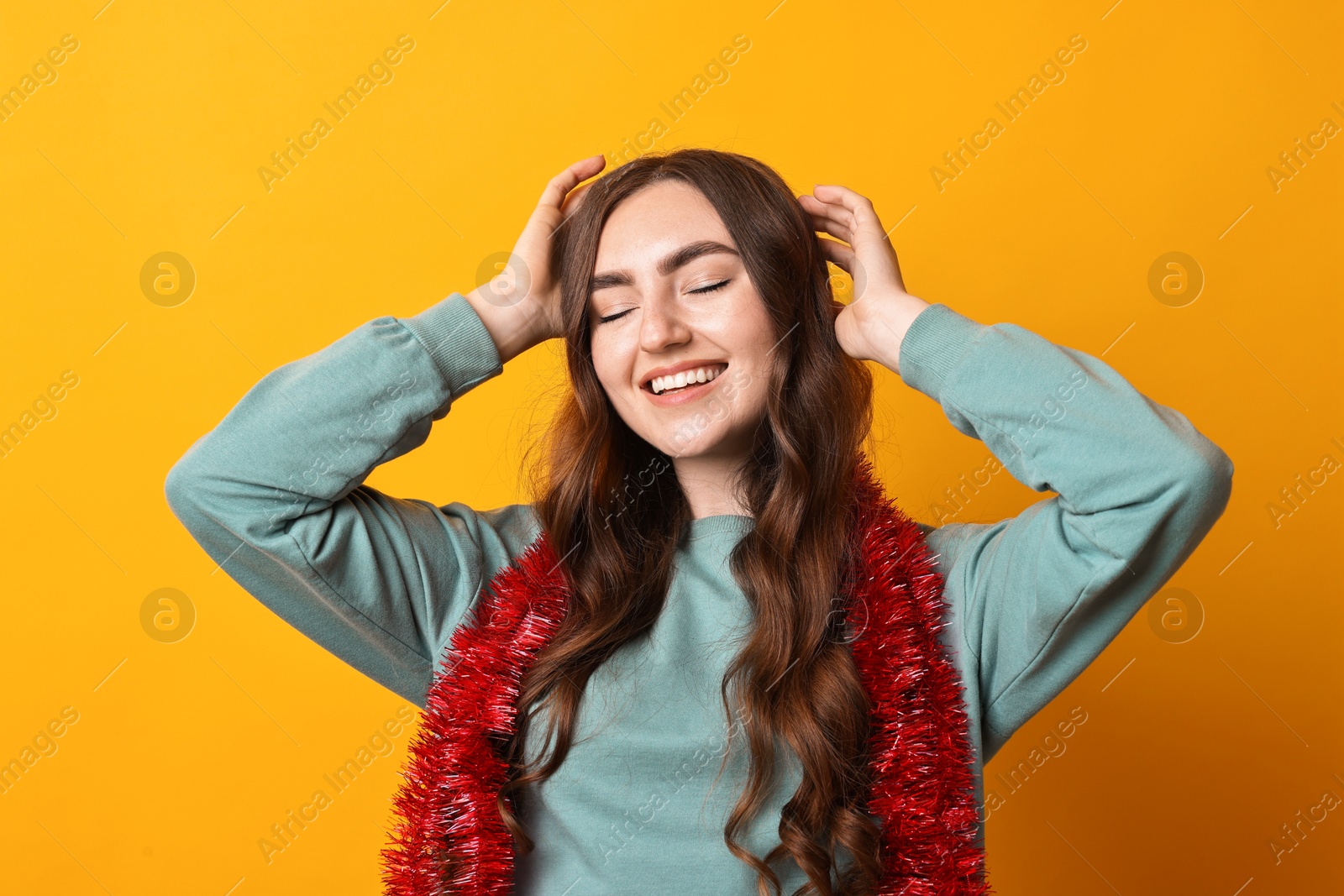 Photo of Happy young woman with tinsel on orange background