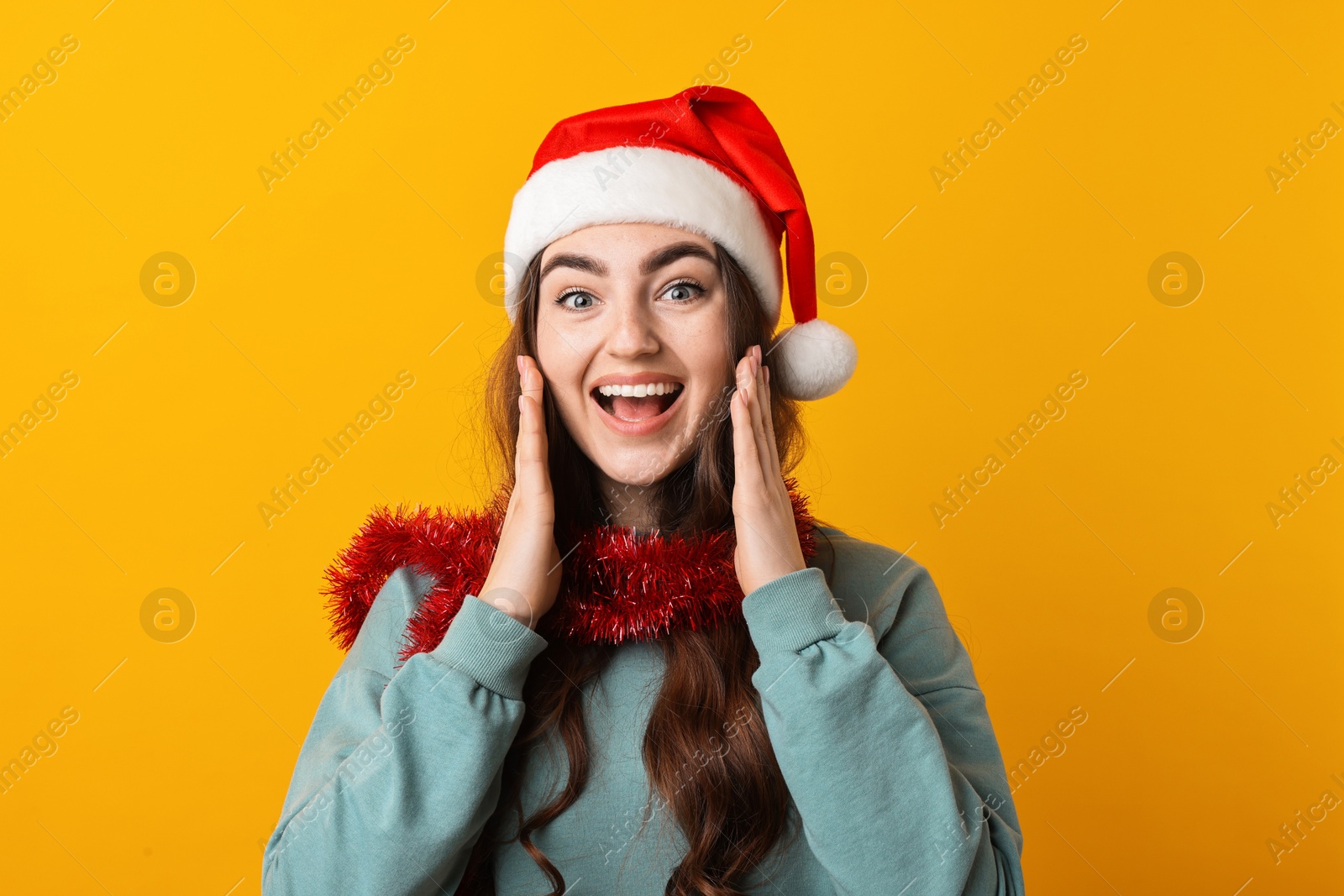 Photo of Emotional young woman with tinsel and Santa hat on orange background