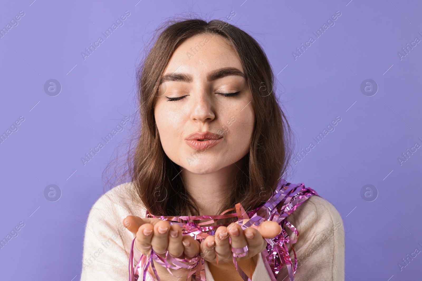 Photo of Young woman with bright tinsel sending air kiss on purple background