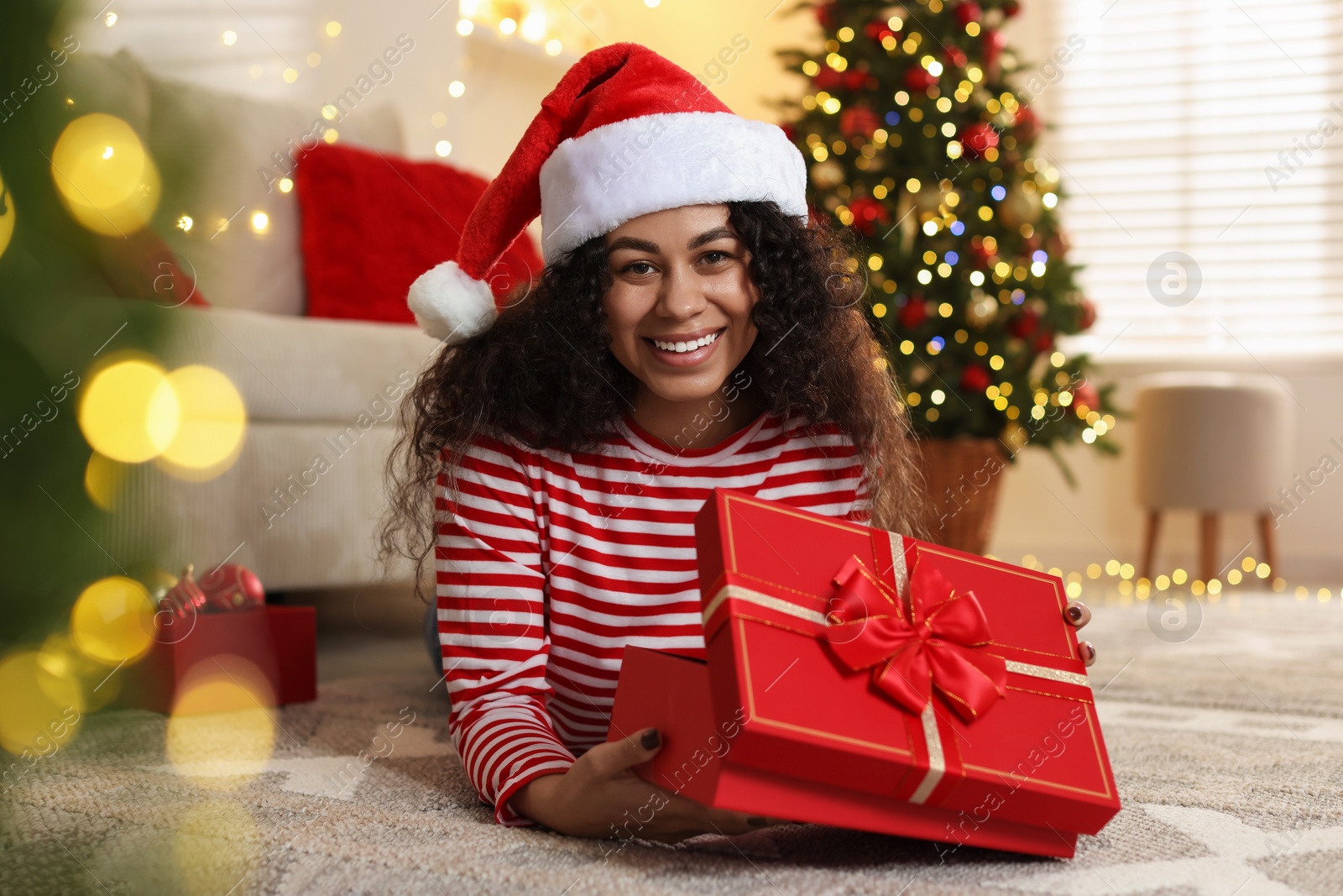 Photo of Happy young woman in Santa hat with Christmas gift at home