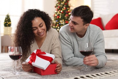 Photo of Happy couple with Christmas gift and glasses of wine spending time together at home