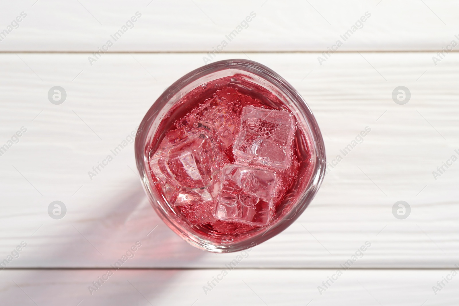 Photo of Sweet soda water with ice cubes in glass on white wooden table, top view