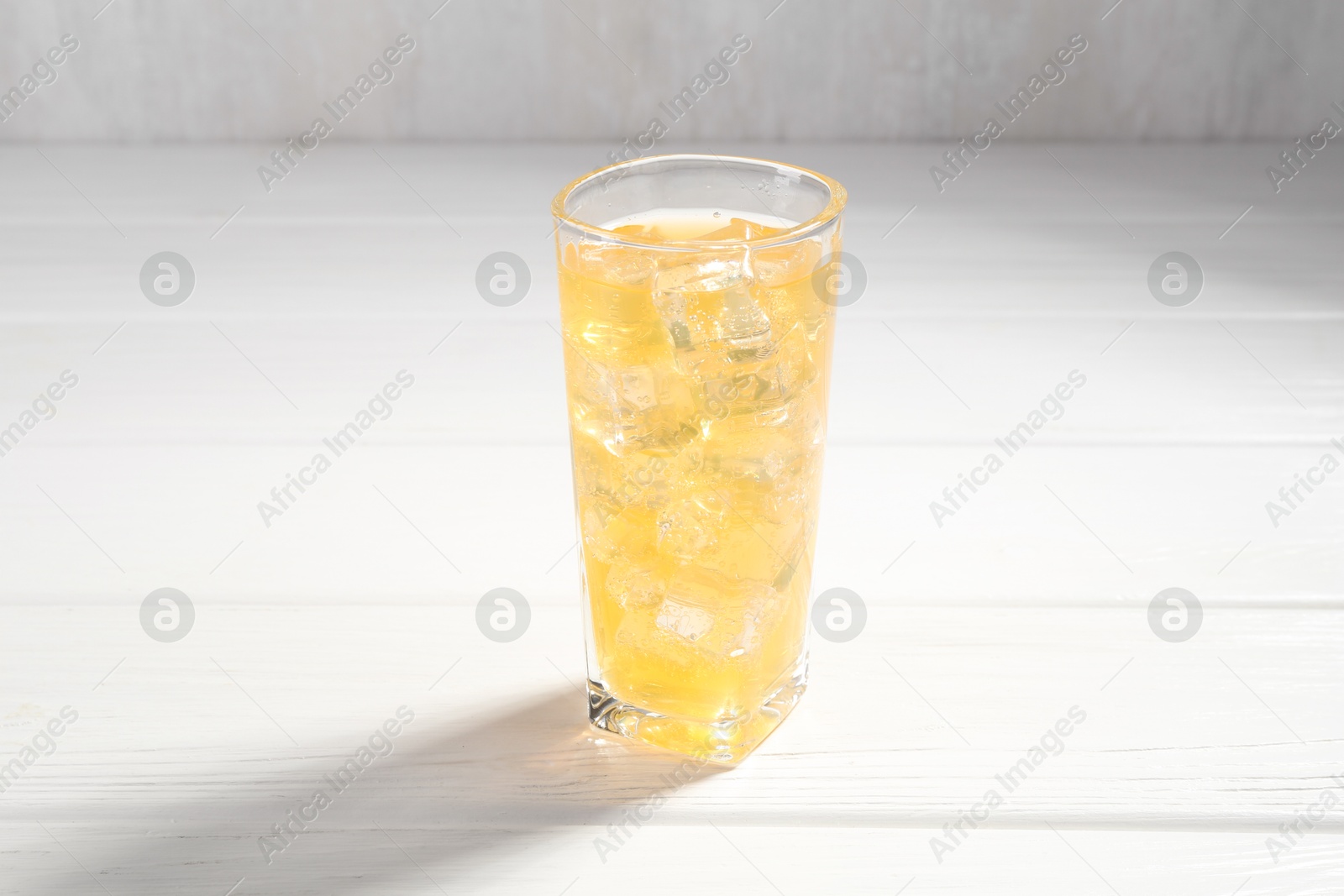 Photo of Sweet soda water with ice cubes in glass on white wooden table