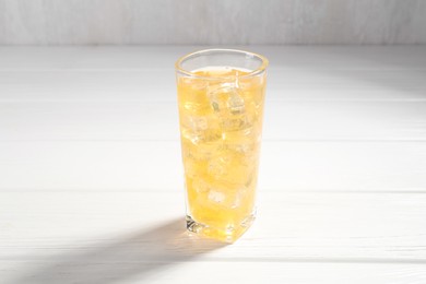 Photo of Sweet soda water with ice cubes in glass on white wooden table