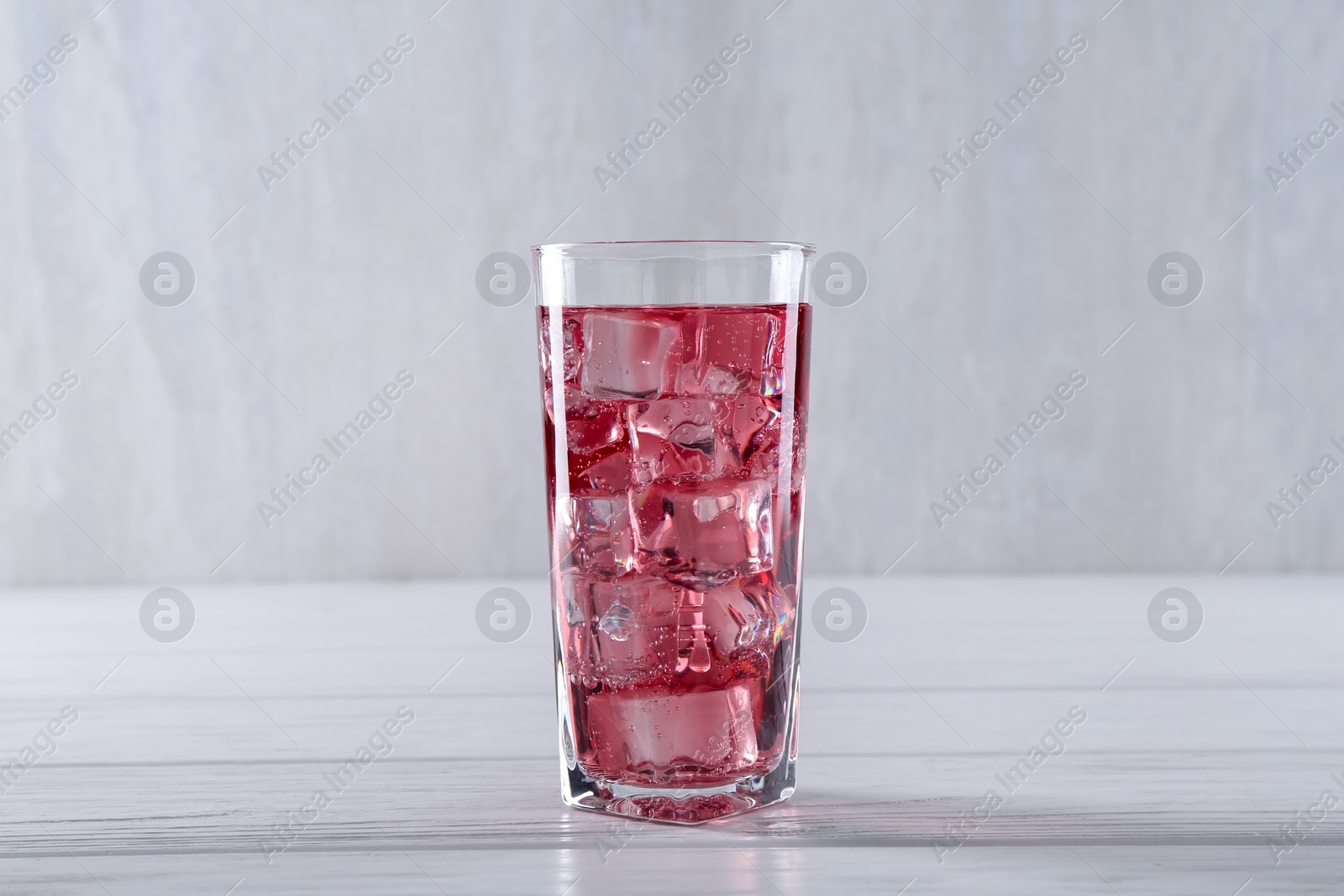 Photo of Sweet soda water with ice cubes in glass on white wooden table