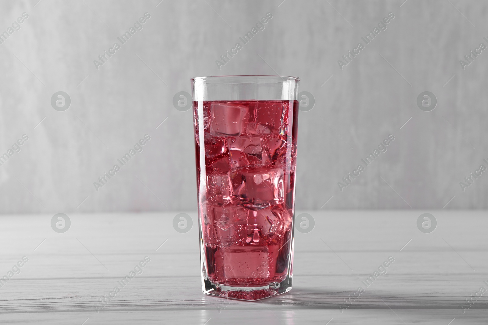 Photo of Sweet soda water with ice cubes in glass on white wooden table