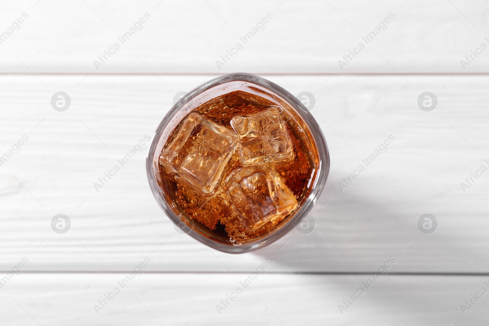 Photo of Sweet soda water with ice cubes in glass on white wooden table, top view