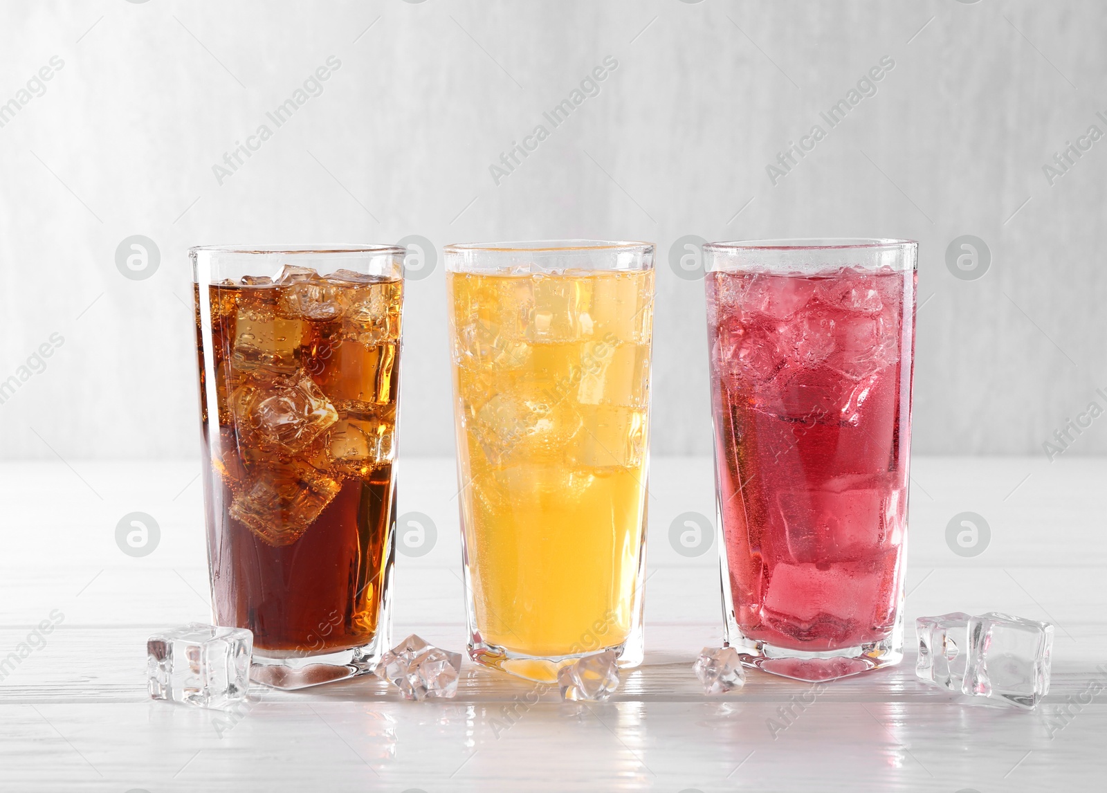 Photo of Soda water of different flavors in glasses with ice cubes on white wooden table