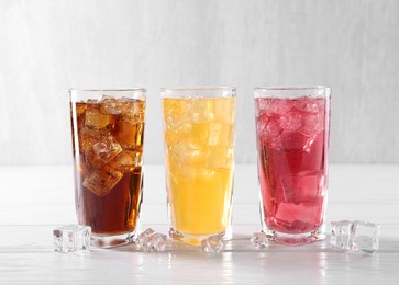 Photo of Soda water of different flavors in glasses with ice cubes on white wooden table