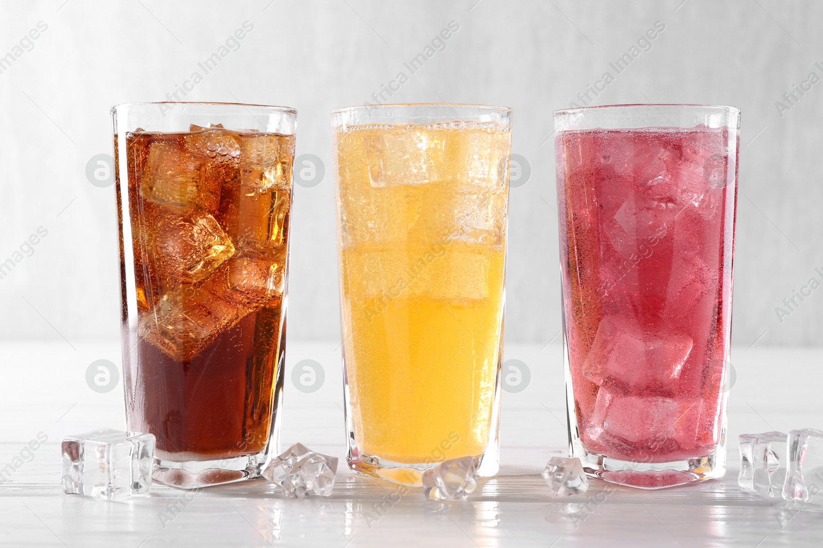 Photo of Soda water of different flavors in glasses with ice cubes on white wooden table