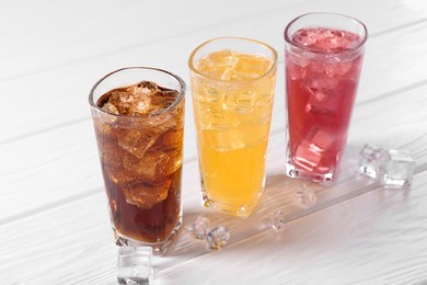 Photo of Soda water of different flavors in glasses with ice cubes on white wooden table