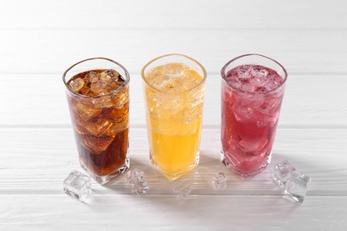 Photo of Soda water of different flavors in glasses with ice cubes on white wooden table