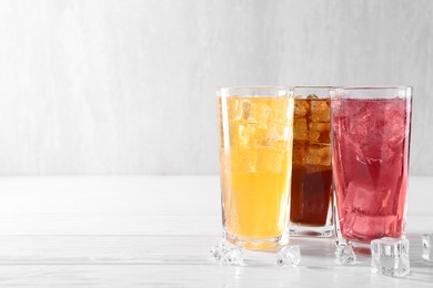 Photo of Soda water of different flavors in glasses with ice cubes on white wooden table, space for text