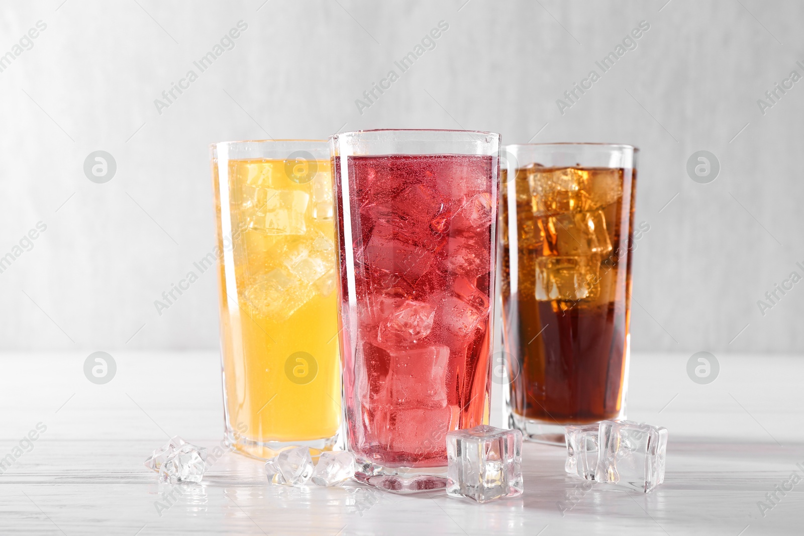 Photo of Soda water of different flavors in glasses with ice cubes on white wooden table