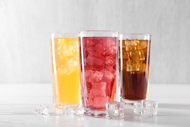 Photo of Soda water of different flavors in glasses with ice cubes on white wooden table