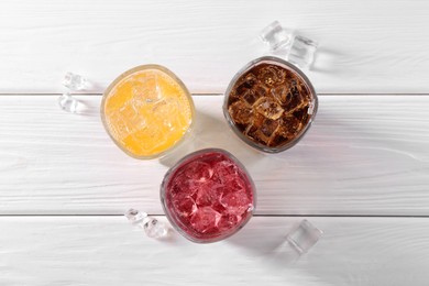 Photo of Soda water of different flavors with ice cubes in glasses on white wooden table, top view