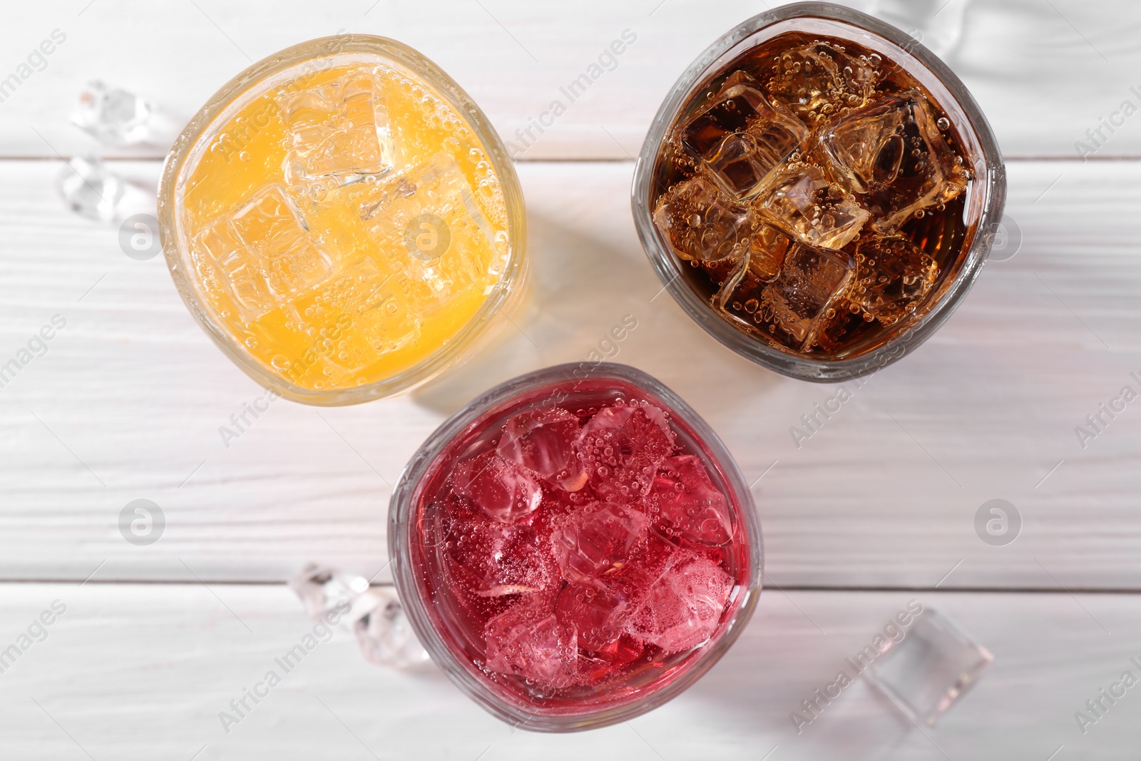 Photo of Soda water of different flavors with ice cubes in glasses on white wooden table, top view