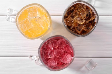 Photo of Soda water of different flavors with ice cubes in glasses on white wooden table, top view